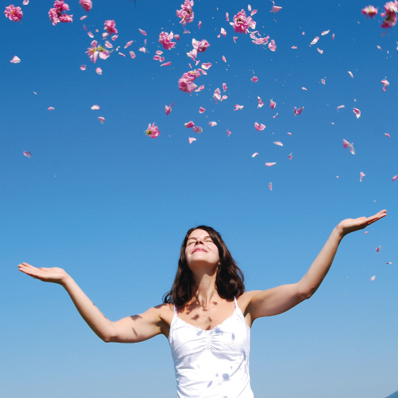 Lächelnde Frau wirft Rosenblätter in die Luft, Symbol für natürliche Pflege